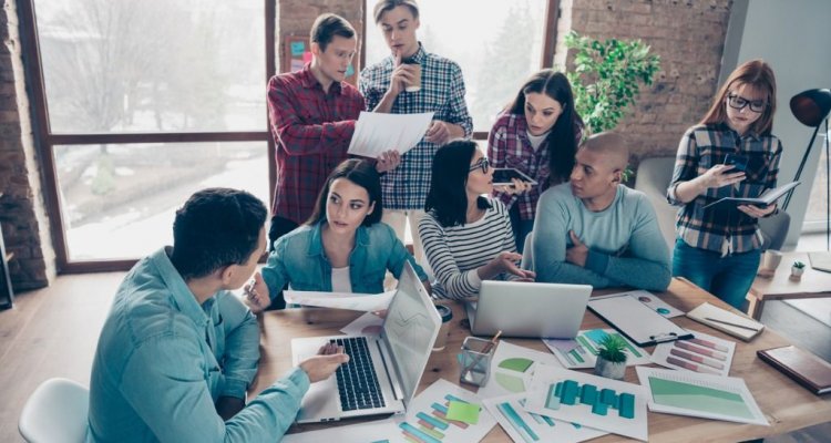 Jovens executivos debatem numa sala planilhas e números de uma organização.