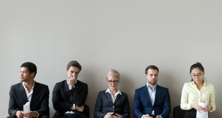 Candidatos sentados em cadeiras esperam ansiosos pela entrevista de emprego.