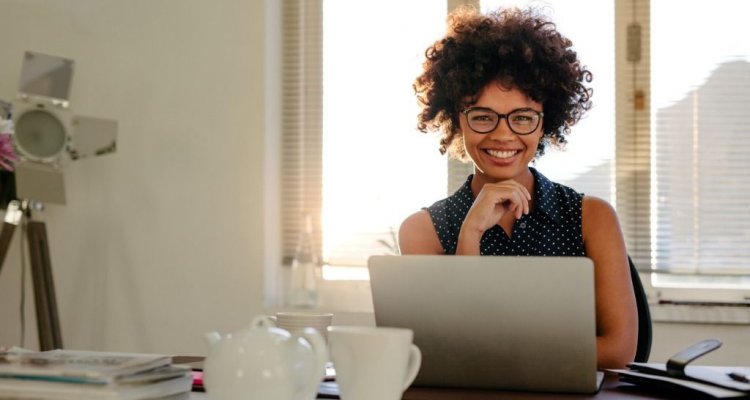 Executiva com óculos à frente de um computador sorrindo.