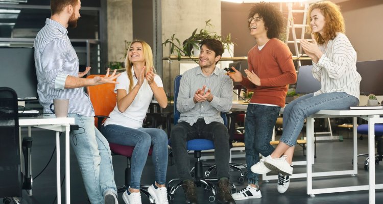 Numa reunião de equipe, jovens executivos aplaudem um colega de trabalho.