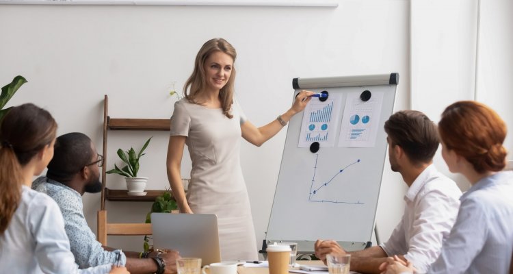 executiva explica números de um dashboard exposto num quadro aos colegas reunidos na mesa