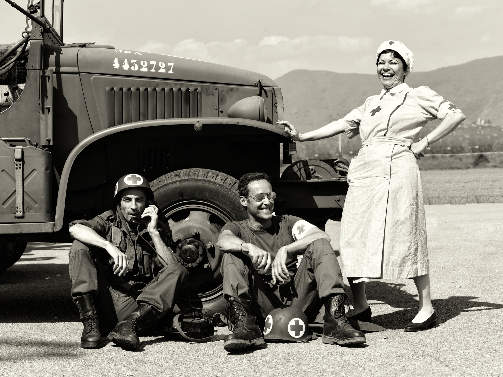 Uma enfermeira sorridente e soldados à frente de um veículo militar da Segunda Guerra Mundial