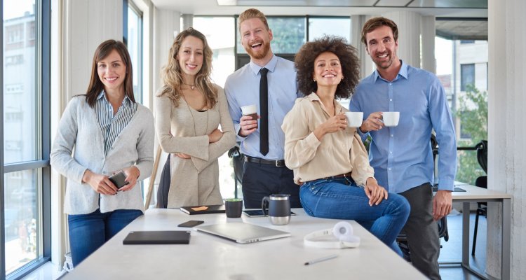 Equipe unida sorrindo em pé na beira da mesa