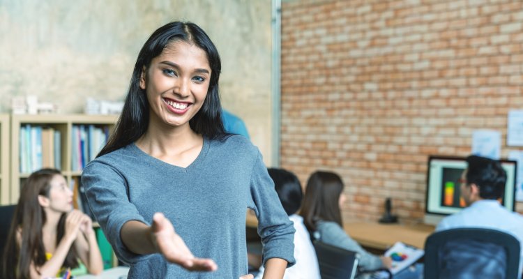 Profissional trans estende a mão ao fundo colegas de trabalho atuam num escritório descolado
