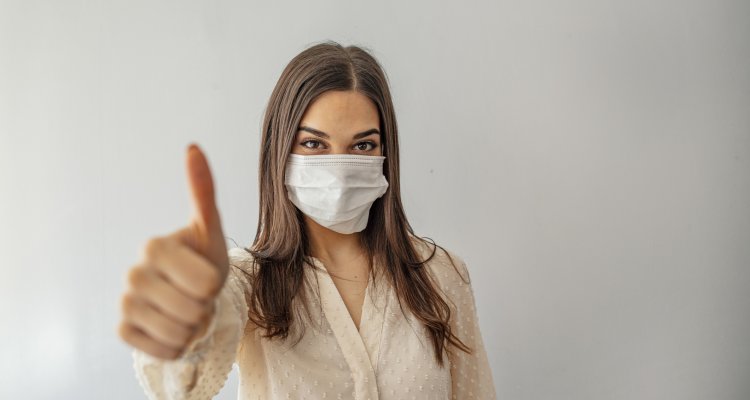 Mulher com máscara mostra o polegar indicando positivo